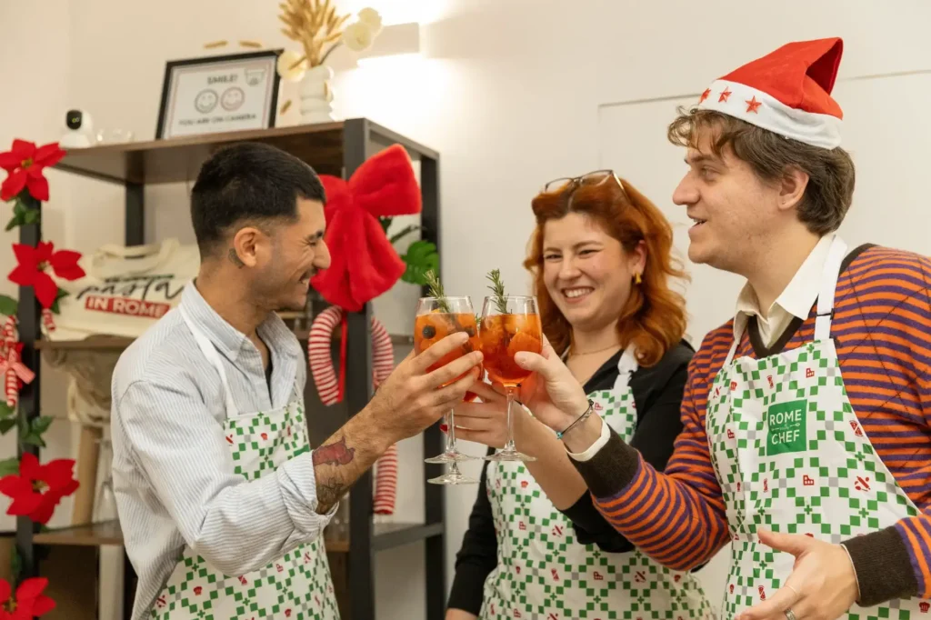 Three cooking class participants in festive attire toasting with homemade Italian aperitif cocktails in a cheerful holiday cooking class celebration